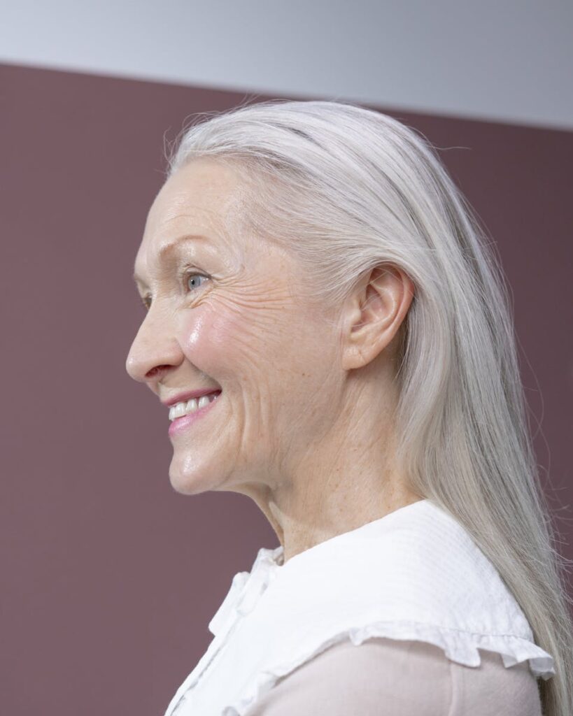 Portrait of a senior woman with gray hair, smiling in profile against a simple background.
